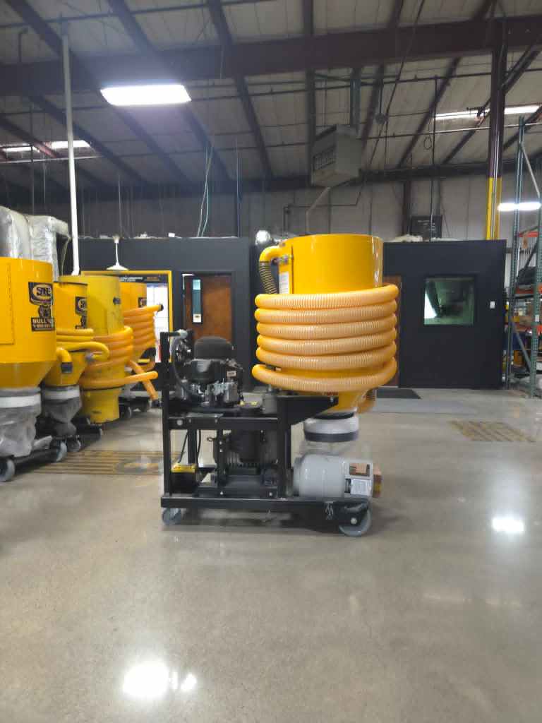 Industrial factory scene with bright yellow machinery and large orange coiled hoses, on a polished concrete floor under overhead lights