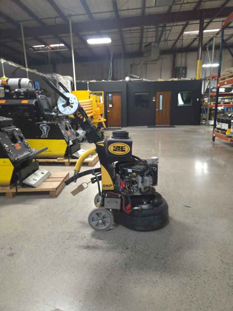 Industrial workshop showing large yellow and black machinery in the foreground, with a dark office-like cabin and shelving in the background.