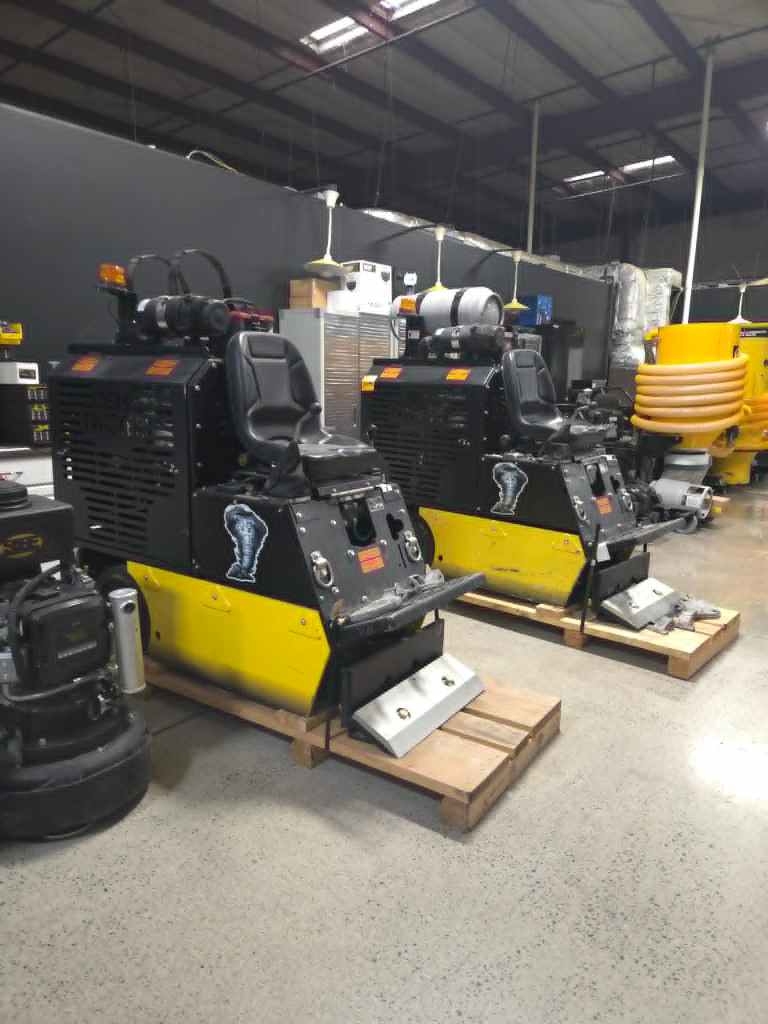 Two large yellow ride-on floor scrubbers with black cabs parked in a warehouse, on wooden pallets with storage cabinets in the background